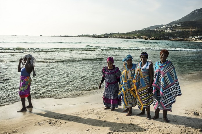 South Africa, Cape Town, Camps Bay. Some women dressed in traditional clothes, walking on the beach after taking part in a wedding. In South African culture, fatness, especially for women, is often associated with health and fertility. Thinness however, is associated with disease and HIV. For this reason, many people do not want to lose weight and adopt a healthier diet. In South Africa, the two-thirds of the population are overweight and the problem affects more women than men: 69.3 percent of South African women have unhealthy levels of body fat and more than four in ten are clinically obese.